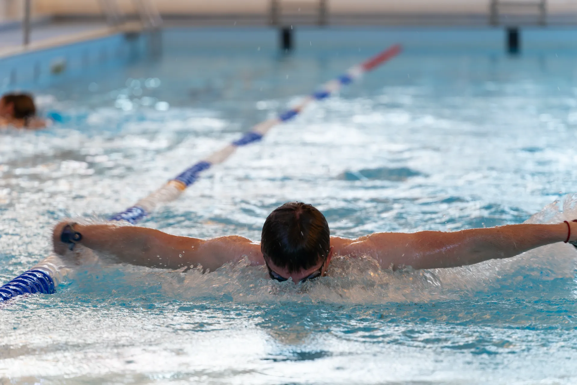 Man in swimming pool doing Butterfly Stroke while lane swimming